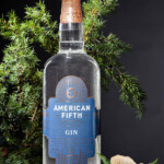 Blue gin in crystal decanter and juniper branch with berries on a black background. Copy space for your text.